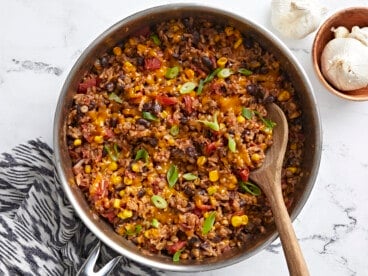 Overhead shot of southwest lentils and rice skillet garnished with green onions and a wooden spoon placed inside the skillet.