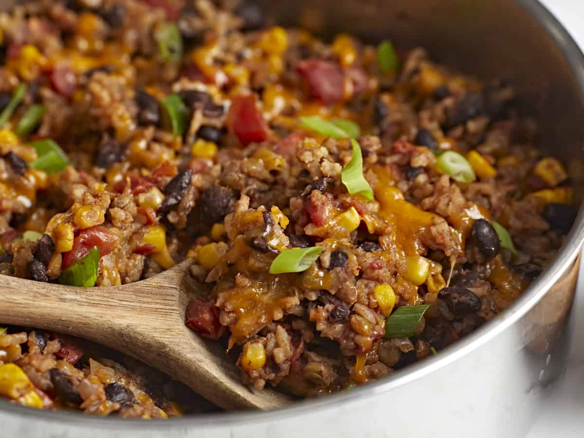 Side front view of southwest lentils and rice skillet with a wooden spoon scooping some out.