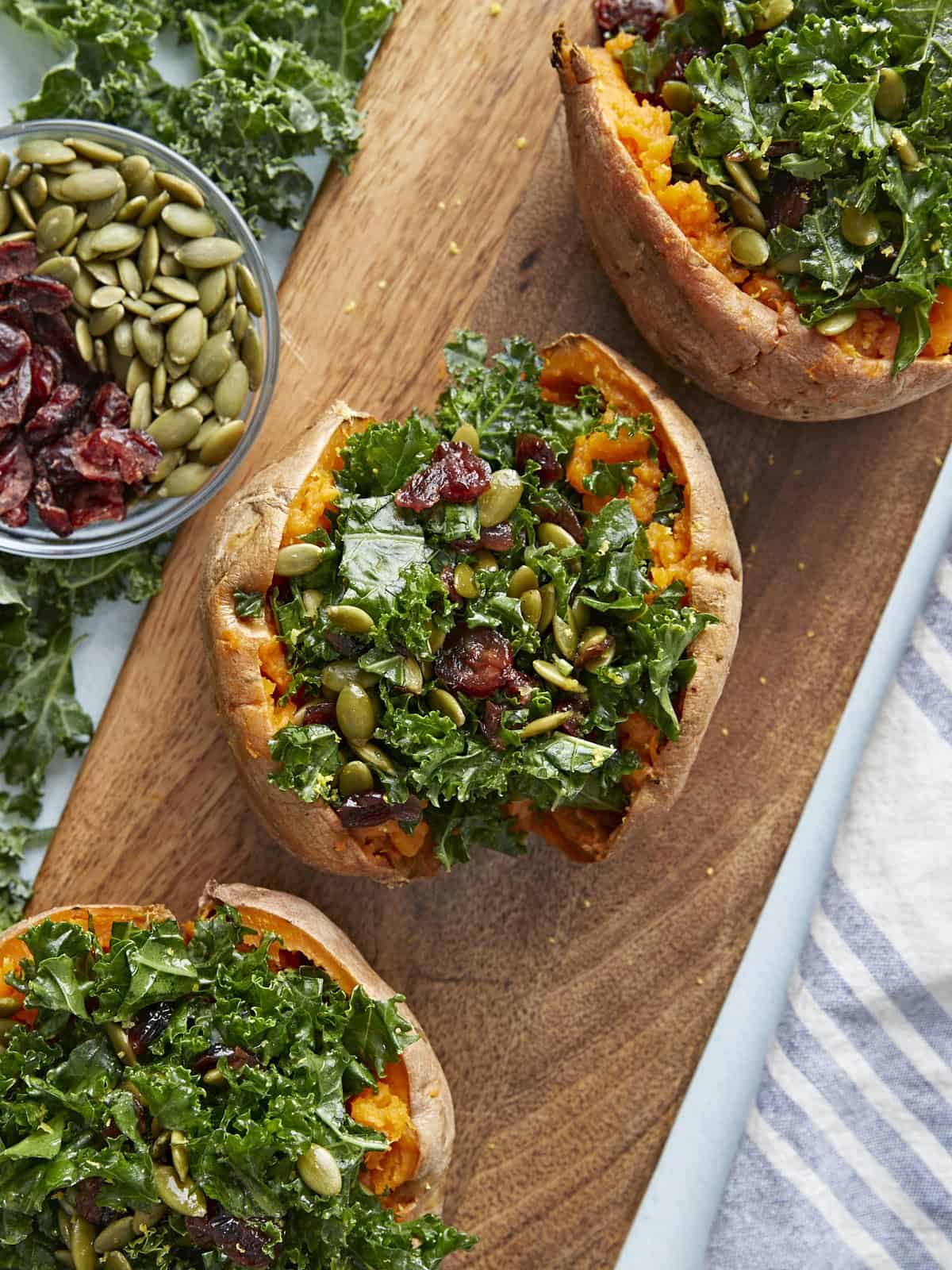 Three stuffed sweet potatoes on a wooden block with cranberries and pepitas on the side.