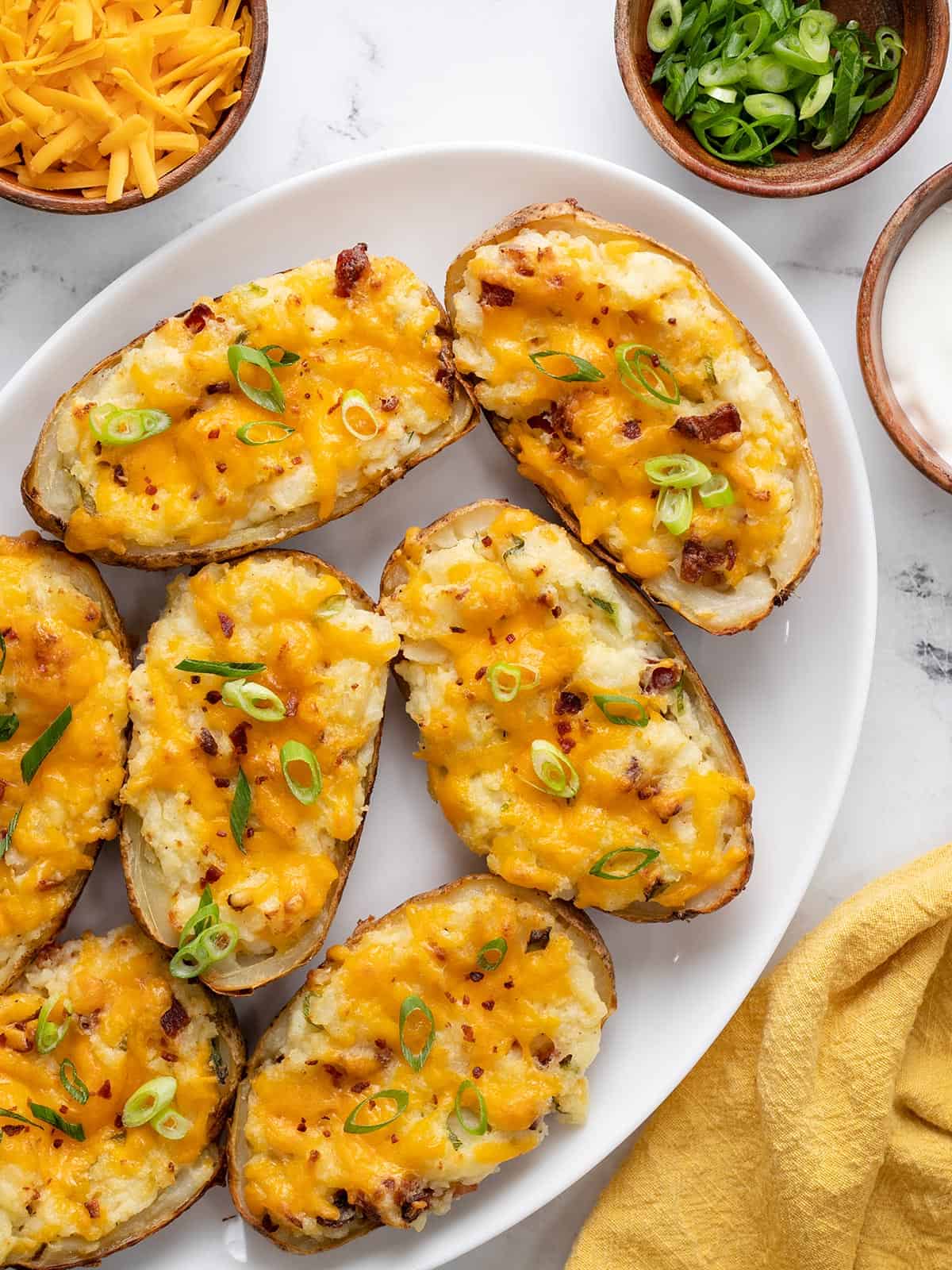 Plated twice baked potatoes with shredded cheese, sliced green onions, and sour cream on the side.