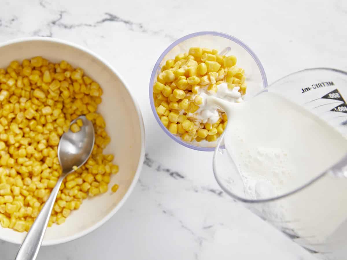 Corn in a blender with half and half being poured in. 