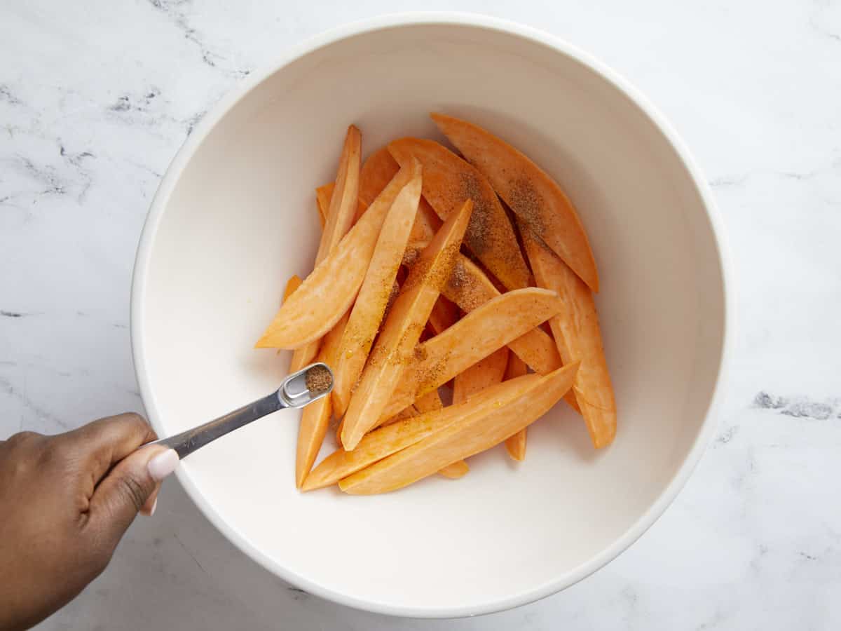 Sweet potato wedges in a large bowl seasoned with olive oil and Creole seasoning.