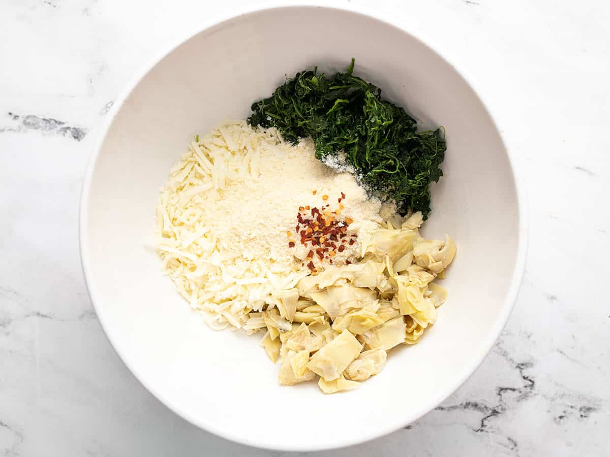 Spinach, artichoke hearts, mozzarella and red pepper in a bowl.