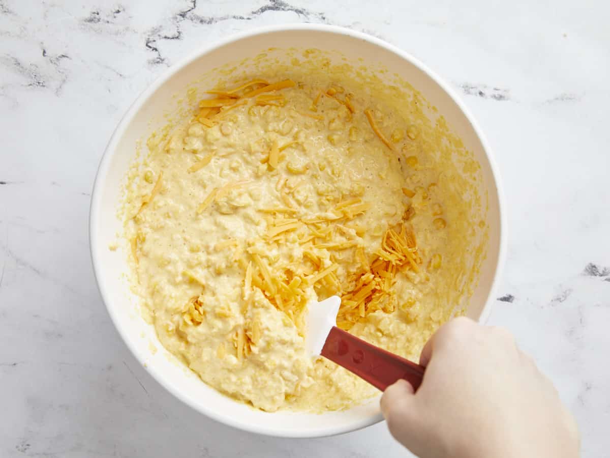 Cheddar cheese being folded into the corn pudding batter.