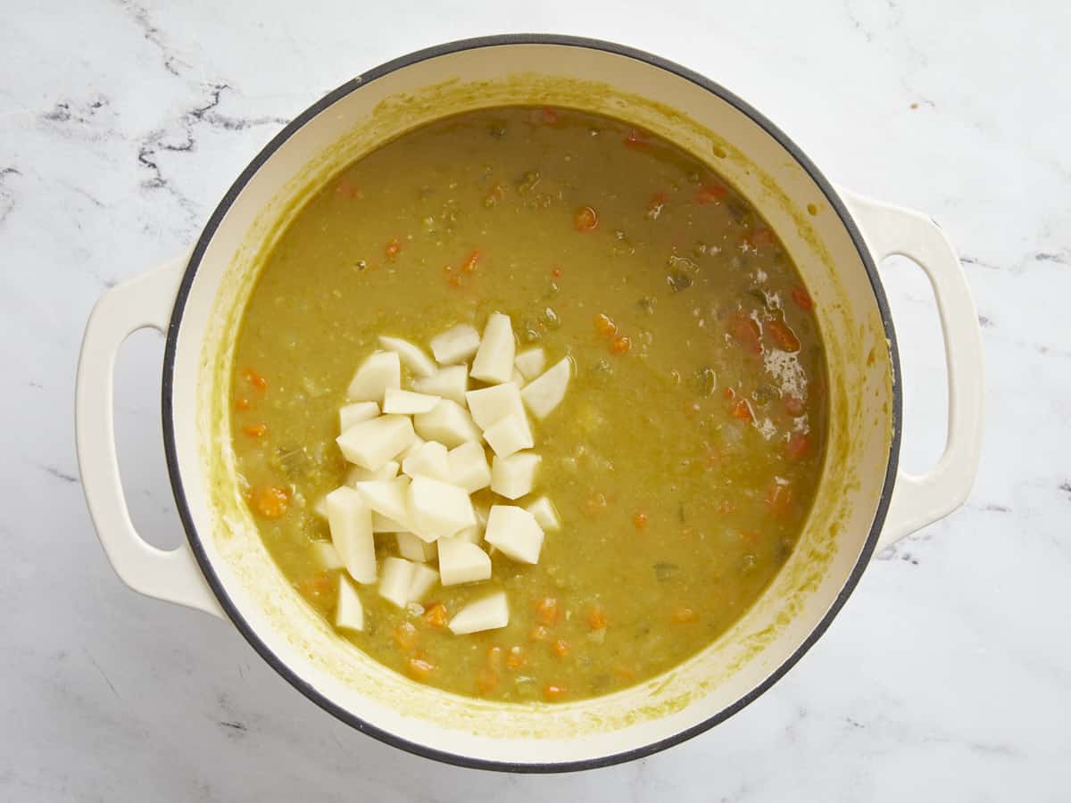 Overhead picture of soup pot with diced potatoes being added and ham hock being removed.