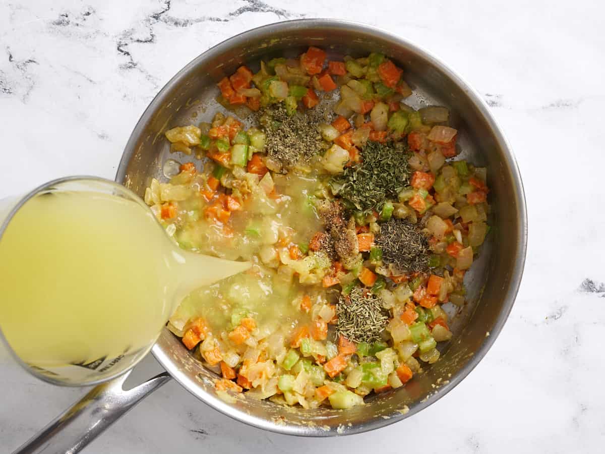 Herbs added to the skillet and broth being poured in the side.