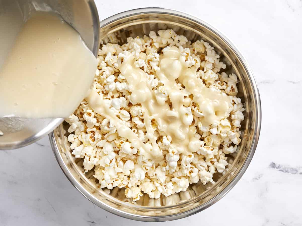 Overhead view of marshmallow sugar mixture being poured over popped popcorn.