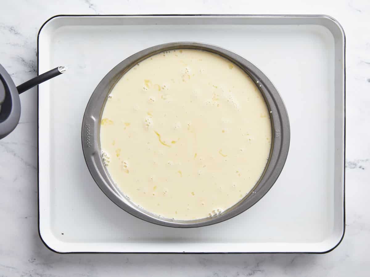 Boiling water being poured into a baking sheet around the cake pan. 