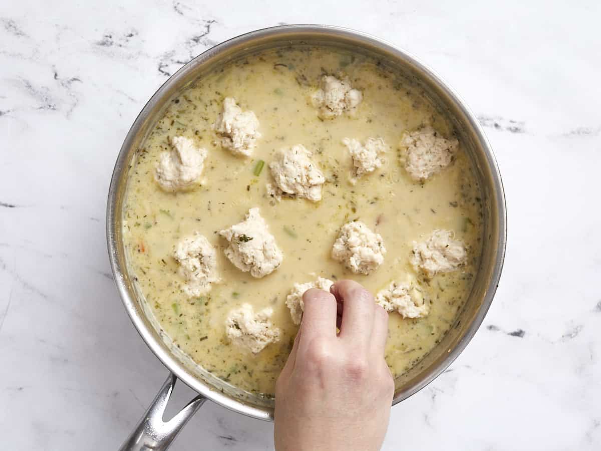 Dumpling dough being dropped into the skillet with the gravy.