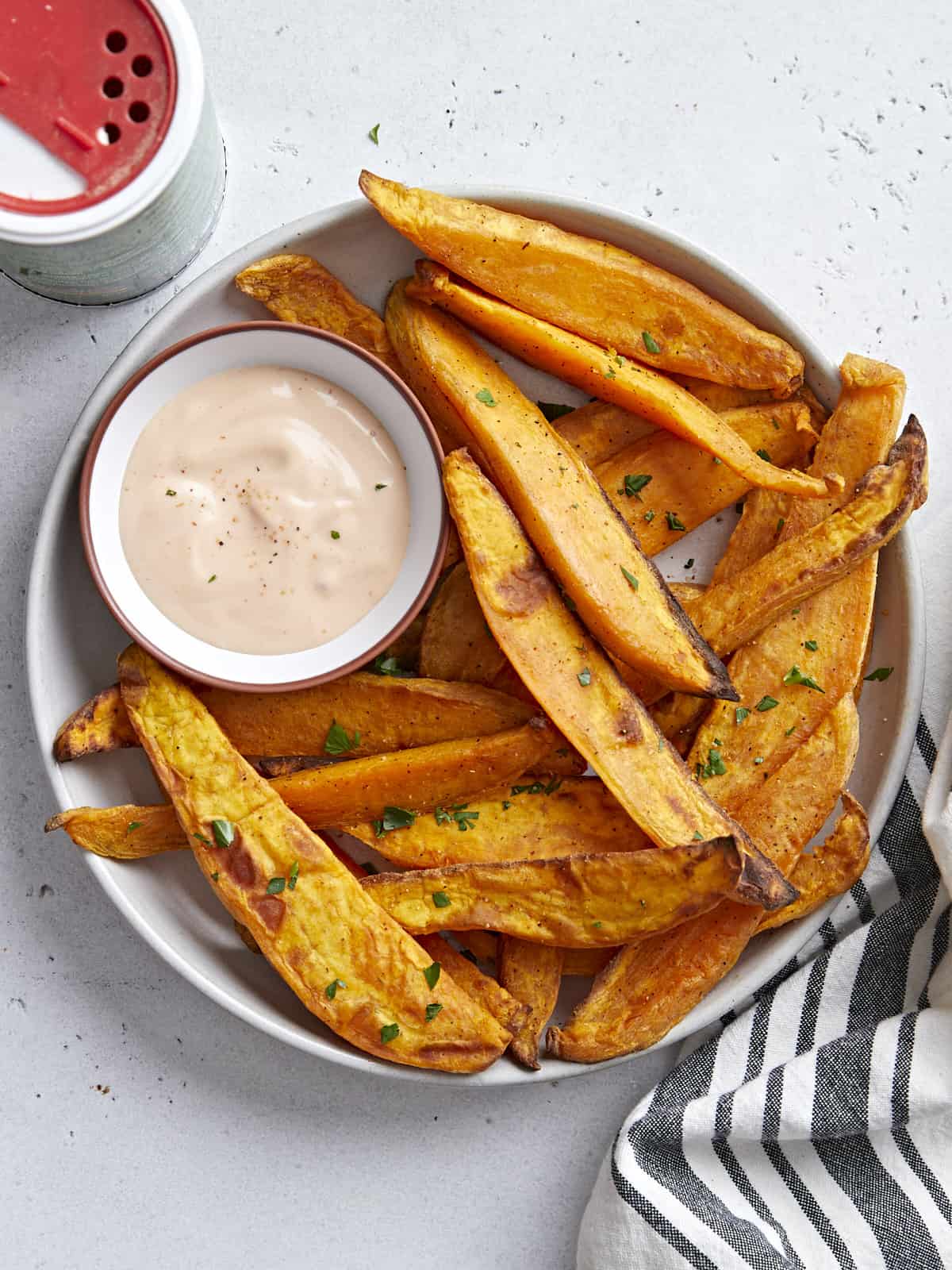 Overhead view of a plate of sweet potato fries served with mayo ketchup dipping sauce and a napkin on the side.