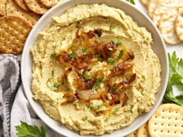 Overhead view of a bowl full of chickpea spread with caramelized onions surrounded by crackers.