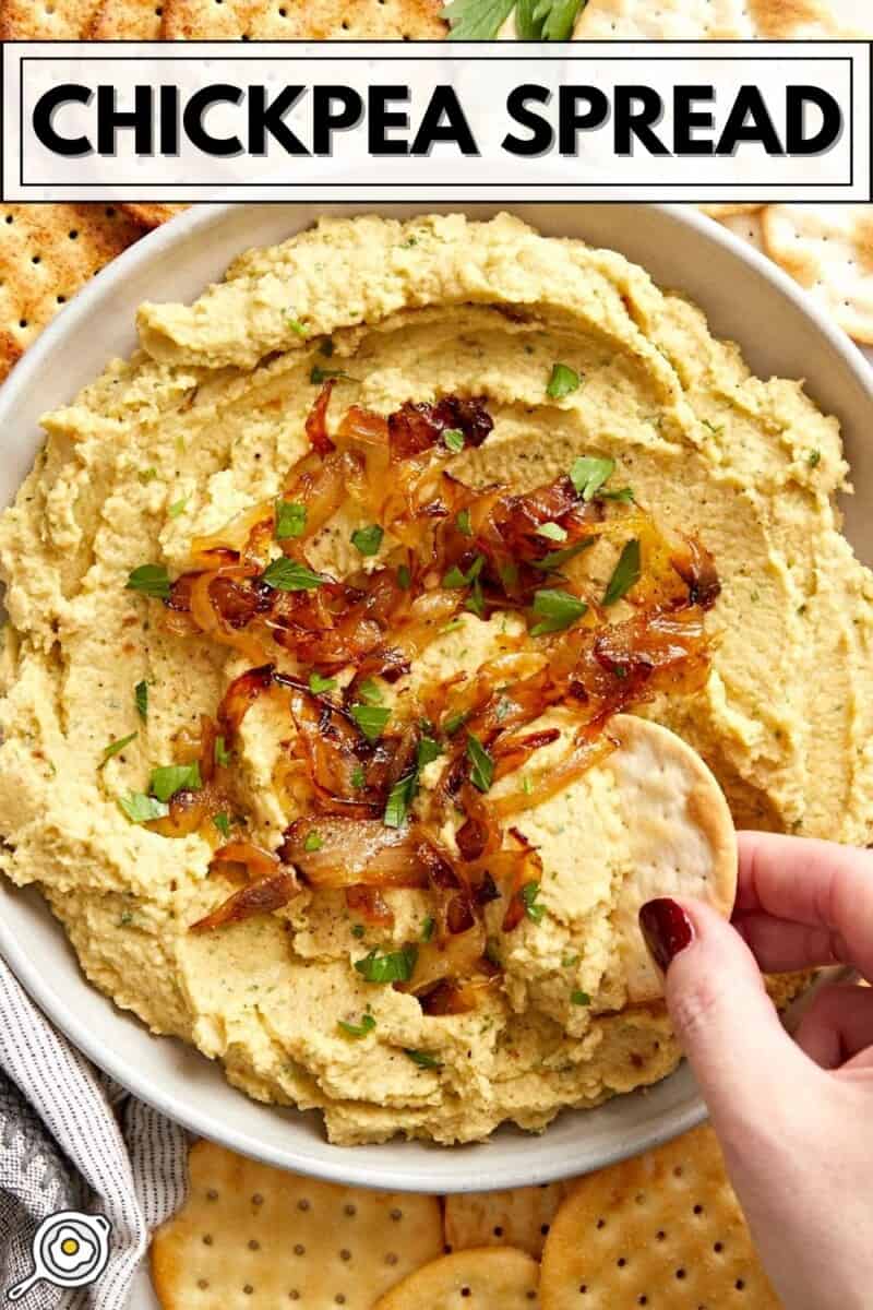 Close up overhead of a cracker being dipped into a bowl of chickpea spread.