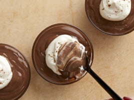 Overhead view of whipped cream being stirred into a cup of pudding.