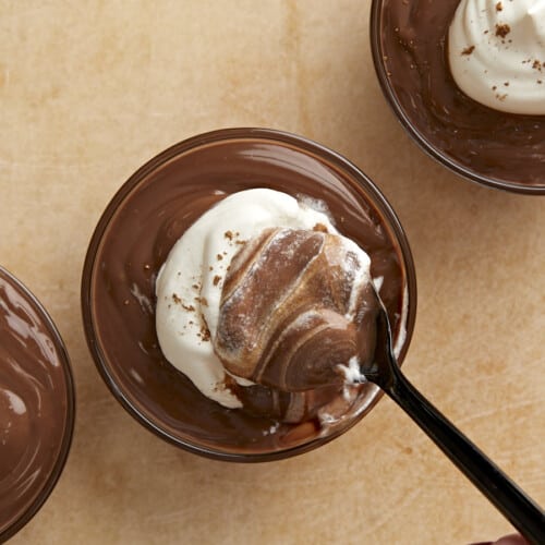 Overhead view of whipped cream being stirred into a cup of pudding.