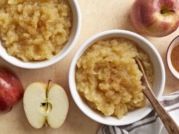 Two small bowls of homemade applesauce with apples and cinnamon on the side.