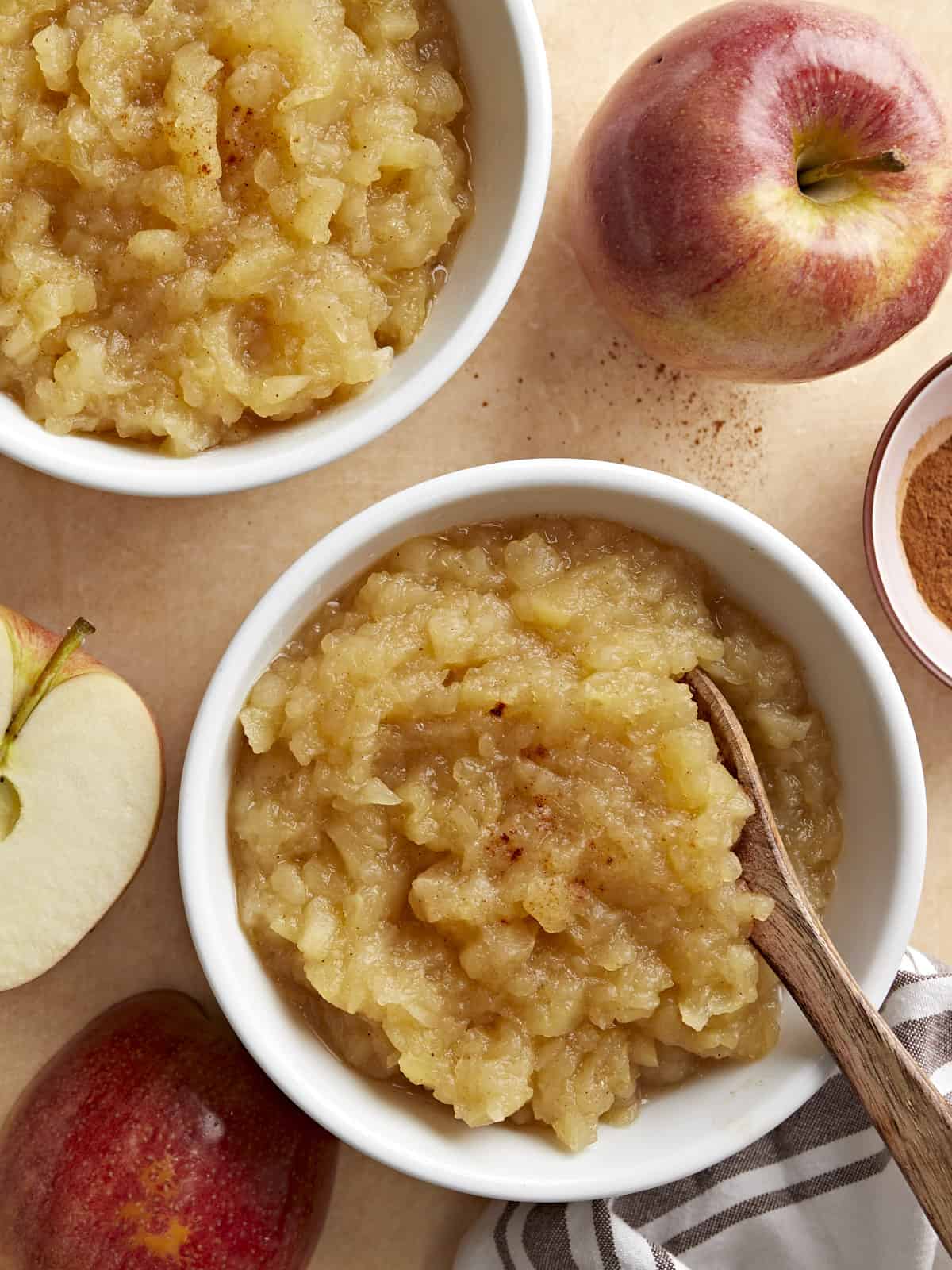 Two small bowls of homemade applesauce with apples and cinnamon on the side.