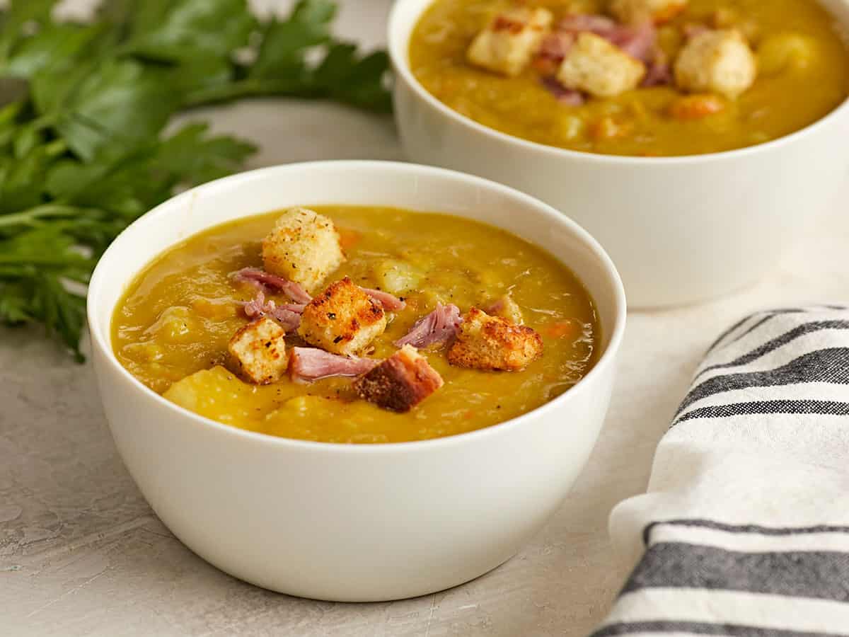 Side view of two bowls of split pea soup with homemade croutons on top.