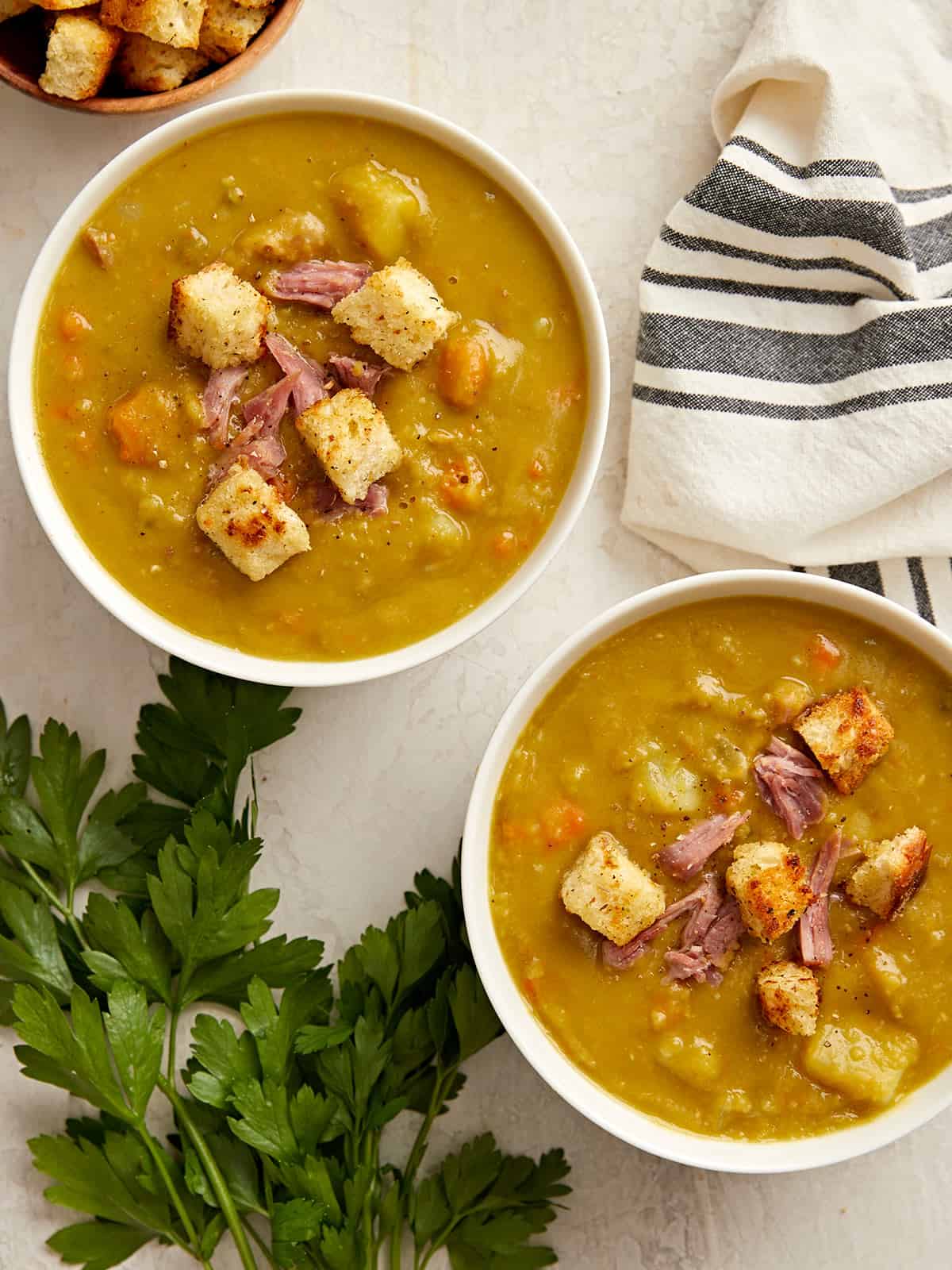 Overhead view of two bowls of split pea soup with parsley and a napkin on the side.