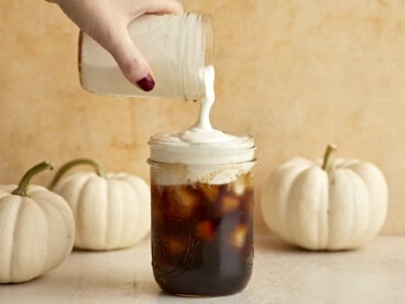 Sweet Cream Cold Foam being poured over a jar full of iced coffee.