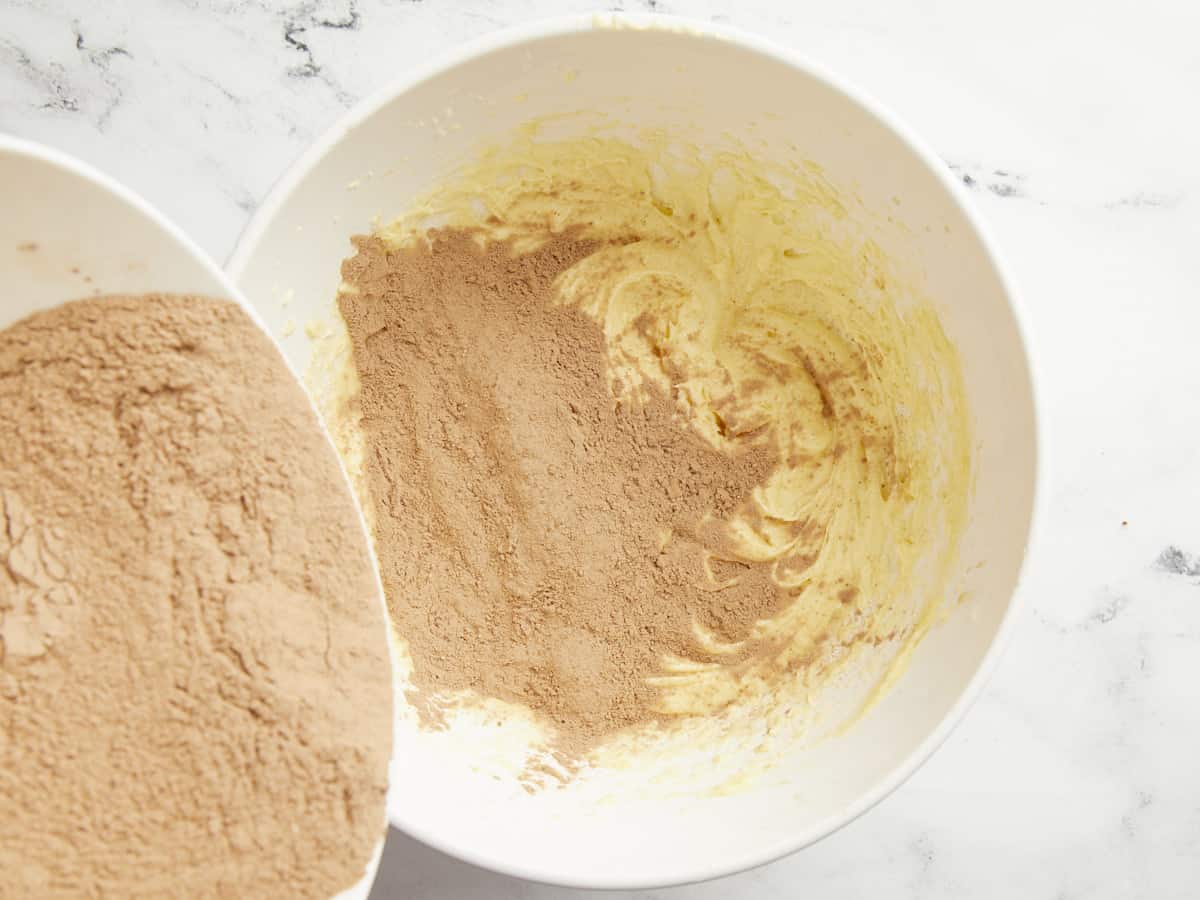 Dry ingredients being poured into the bowl with the butter and eggs. 