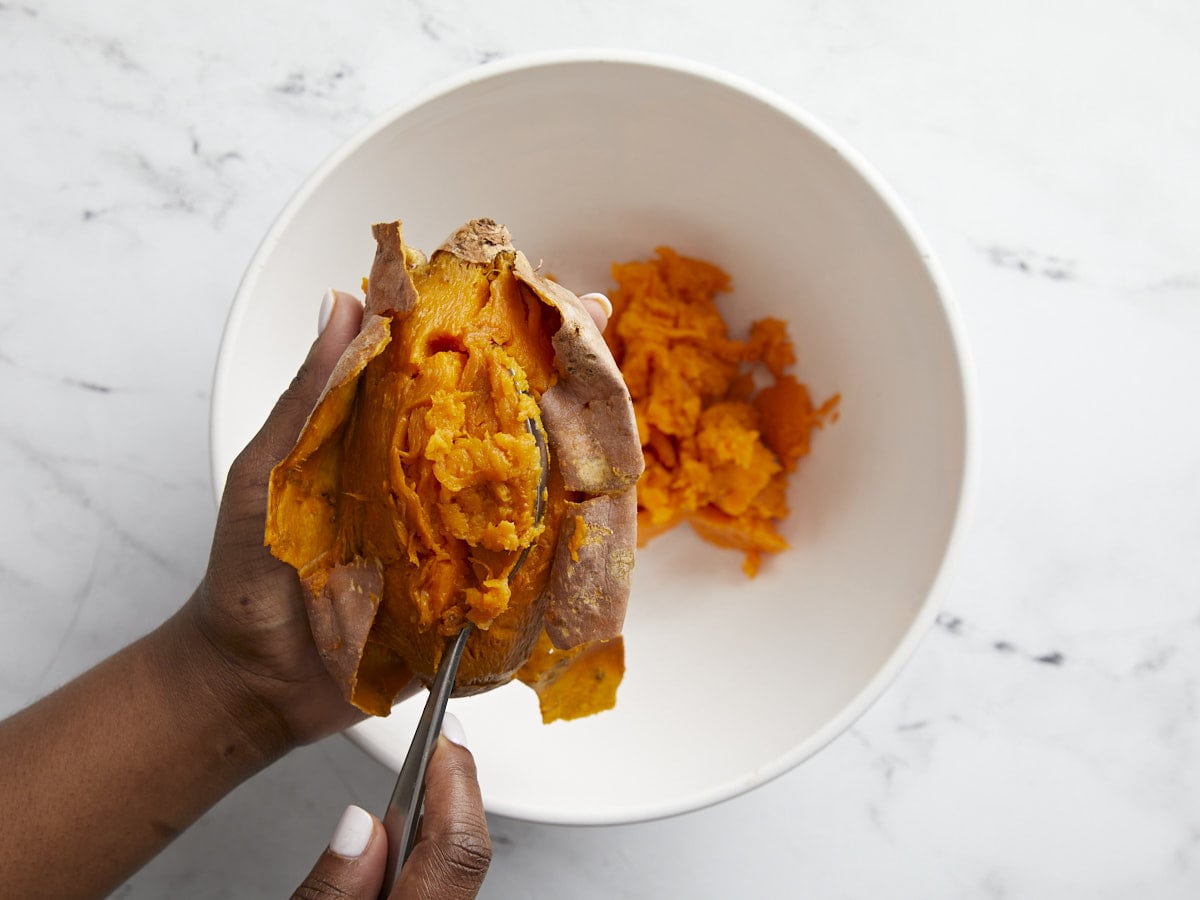 Cooked sweet potato flesh being scooped out of the baked sweet potatoes