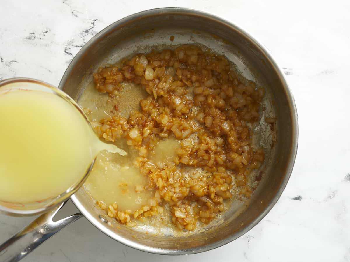 Chicken broth being added to sauteed onions, garlic and cooked flour.