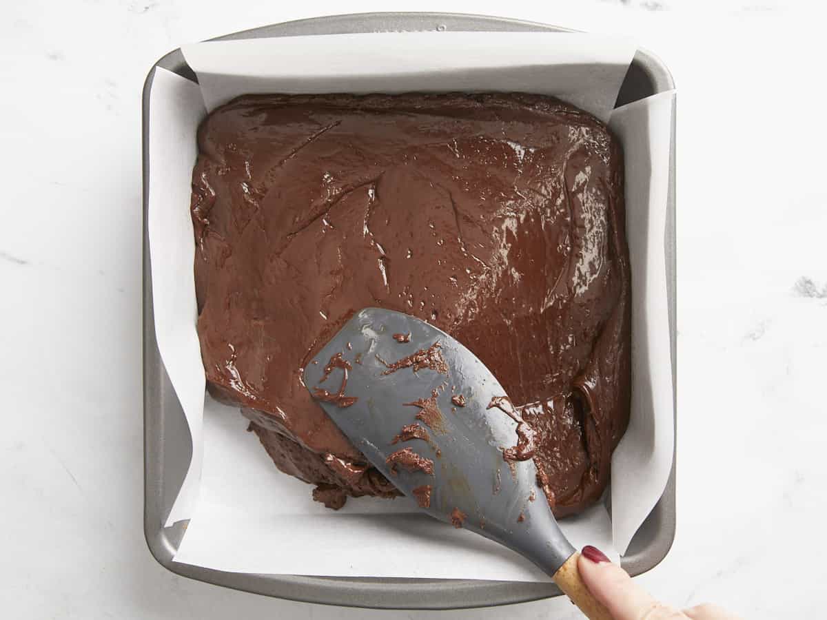 Fudge being spread into a lined baking dish. 