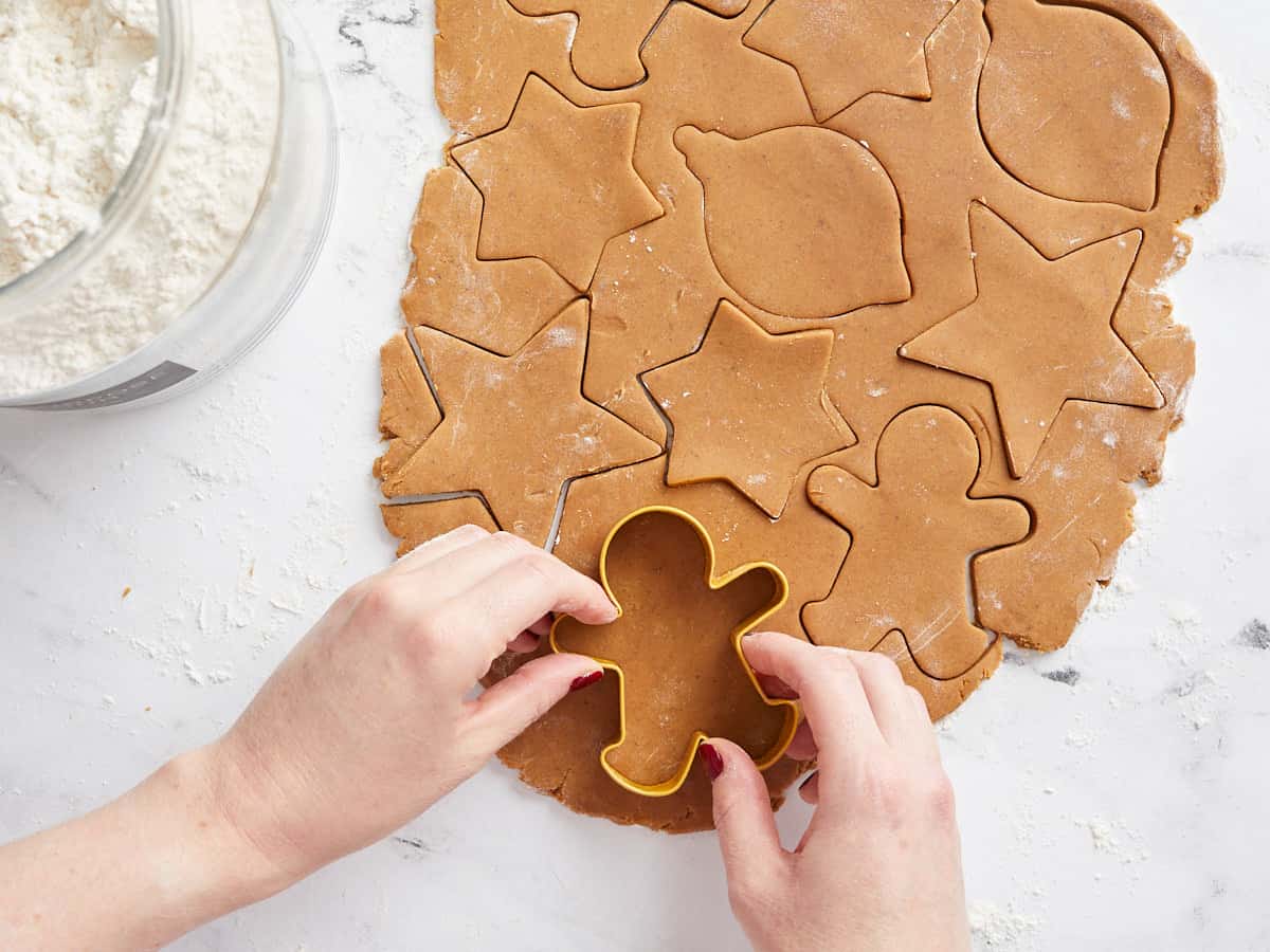 Gingerbread cookie batter rolled out and being cut with a cookie cutter. 