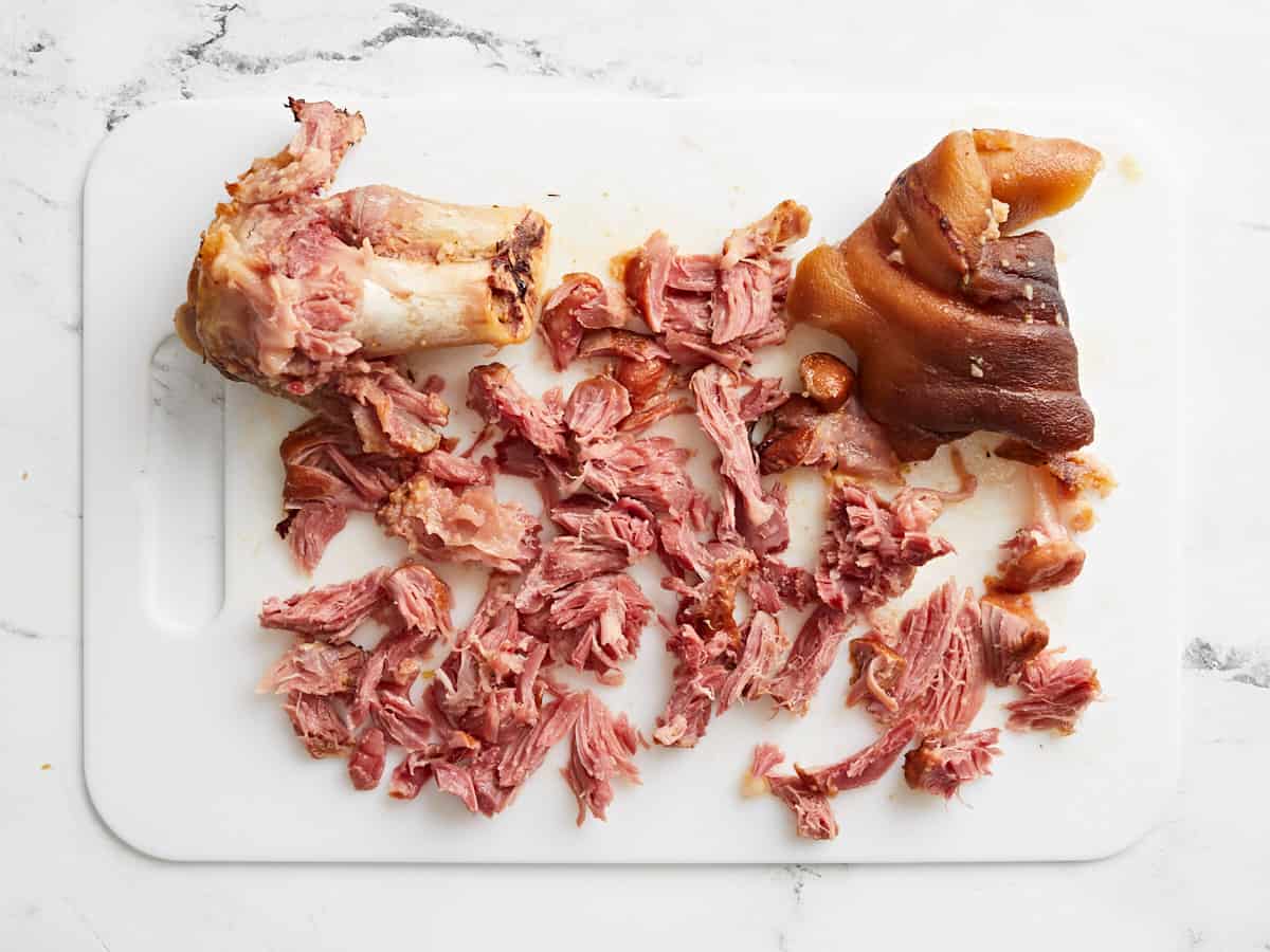 Hamhock meat being removed from the bone on a cutting board.