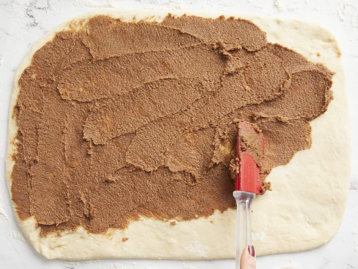 Cinnamon sugar mixture being spread onto the rolled out dough. 