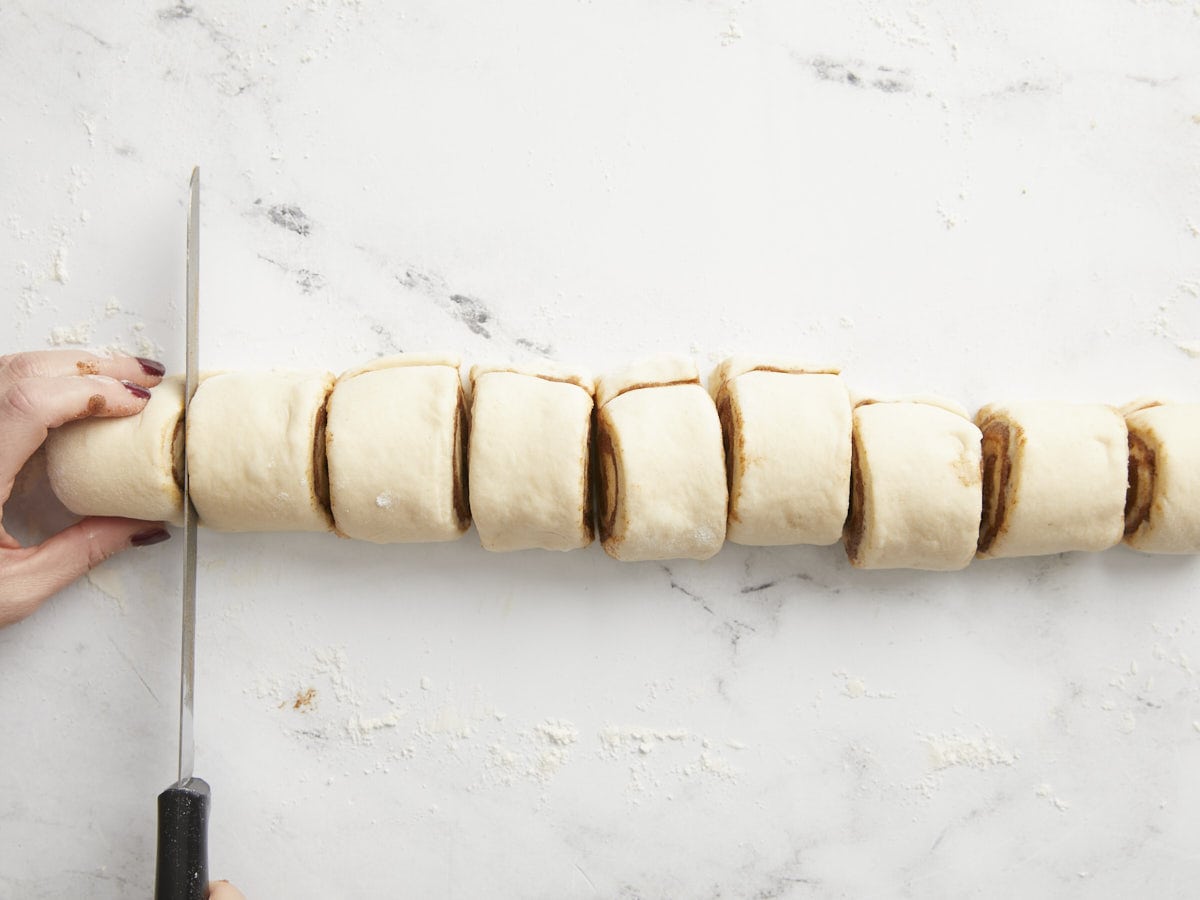 Rolled dough being sliced into rounds. 