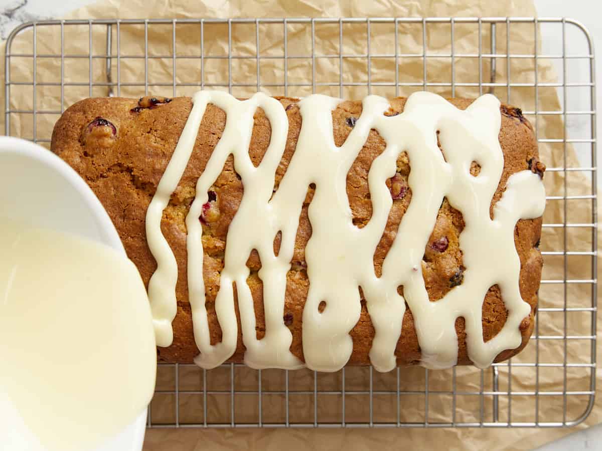 Icing being poured over the cranberry orange bread. 