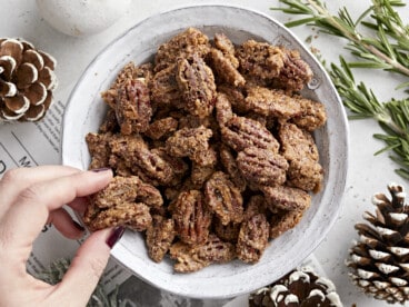 Overhead view of a bowl full of candied pecans and a hand grabbing a few.