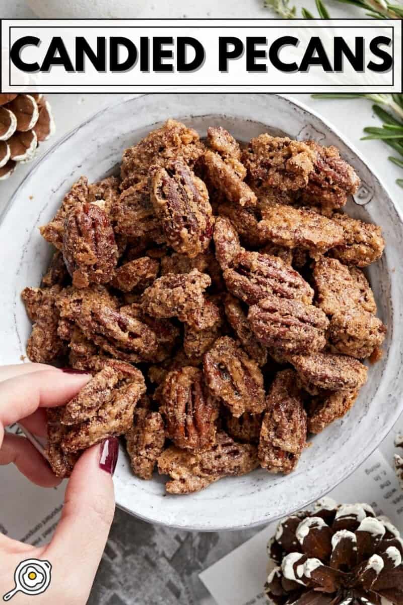 Overhead view of a bowl full of candied pecans with a hand grabbing a couple.