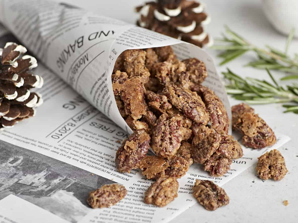 A paper cone filled with candied pecans that are spilling out.