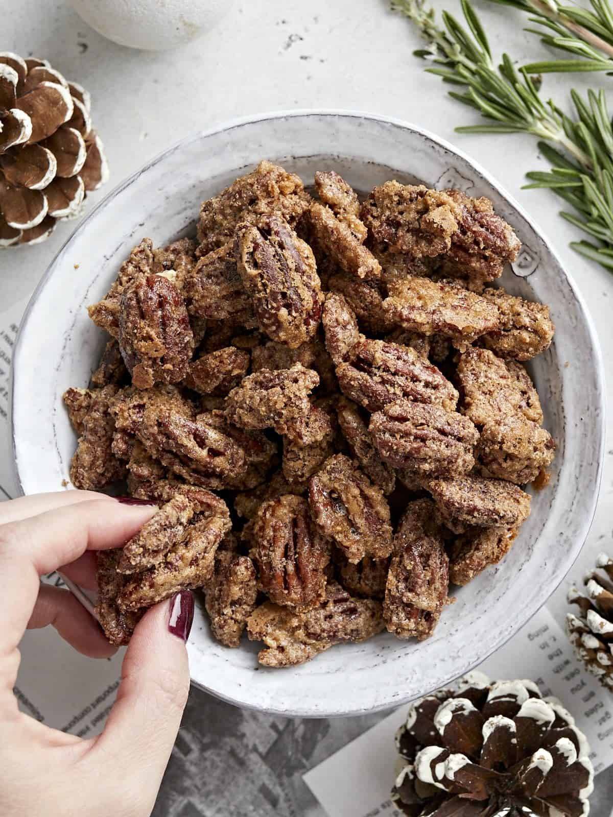 Overhead view of a bowl full of candied pecans with a hand grabbing one.