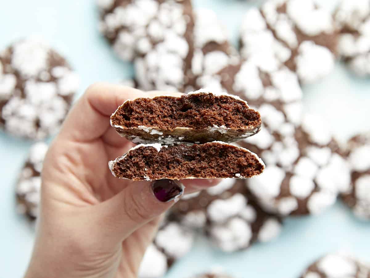 A hand holding a chocolate crinkle cookie that has been broken in half.