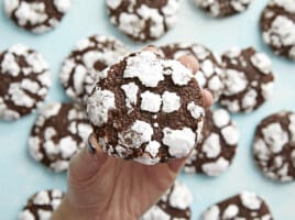 A hand holding a chocolate crinkle cookie close to the camera with others in the background