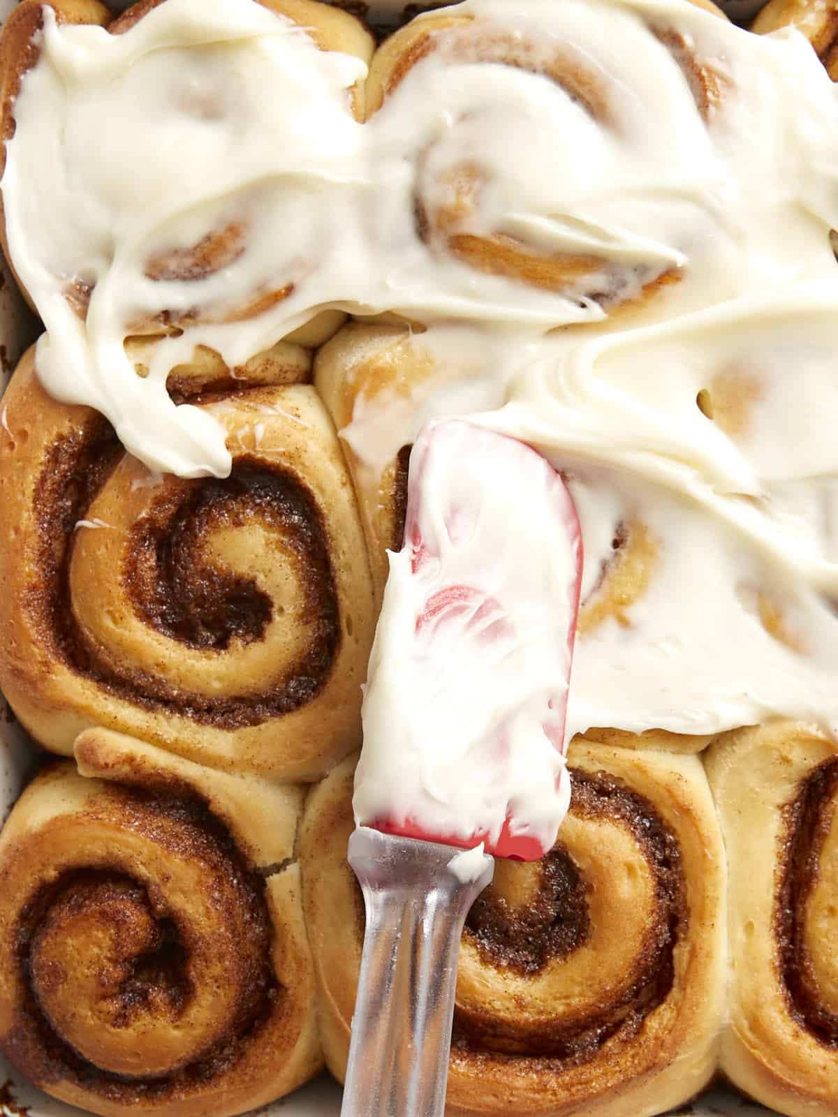 Overhead view of frosting being spread onto homemade cinnamon rolls.