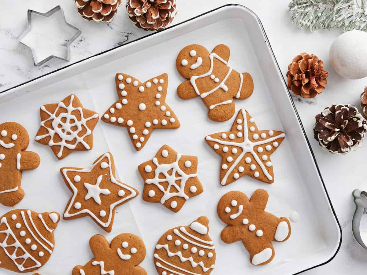 Overhead view of decorated gingerbread cookies on a baking sheet with pinecones on the sides.