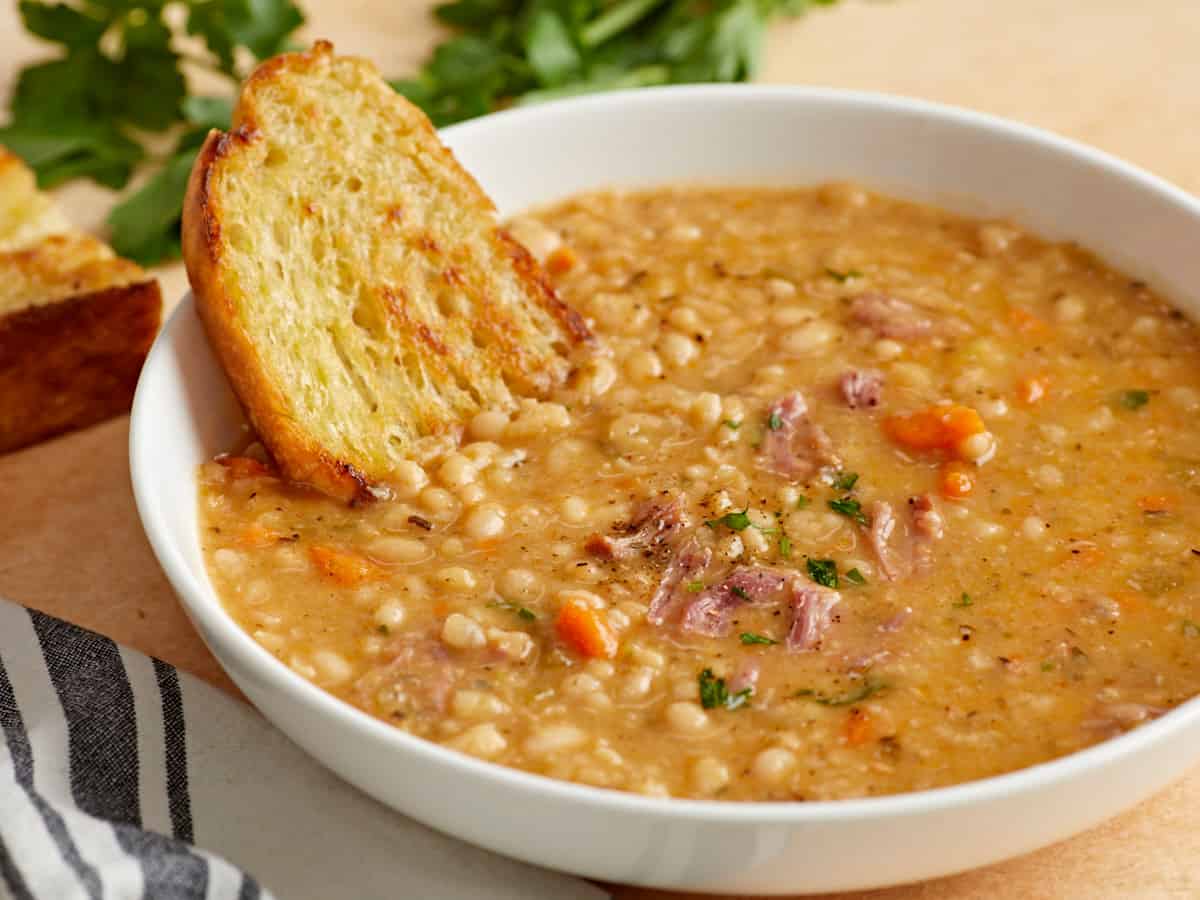 Side view of a bowl full of navy bean soup with crusty bread on the side of the bowl.