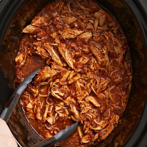 Close overhead view of salsa chicken in the crock pot with tongs.