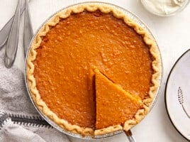 Overhead view of a whole sweet potato pie with one slice cut and being lifted out of the pie pan.