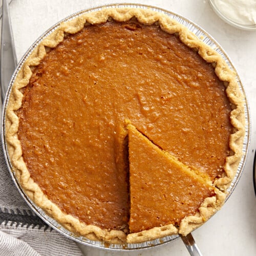 Overhead view of a whole sweet potato pie with one slice cut and being lifted out of the pie pan.