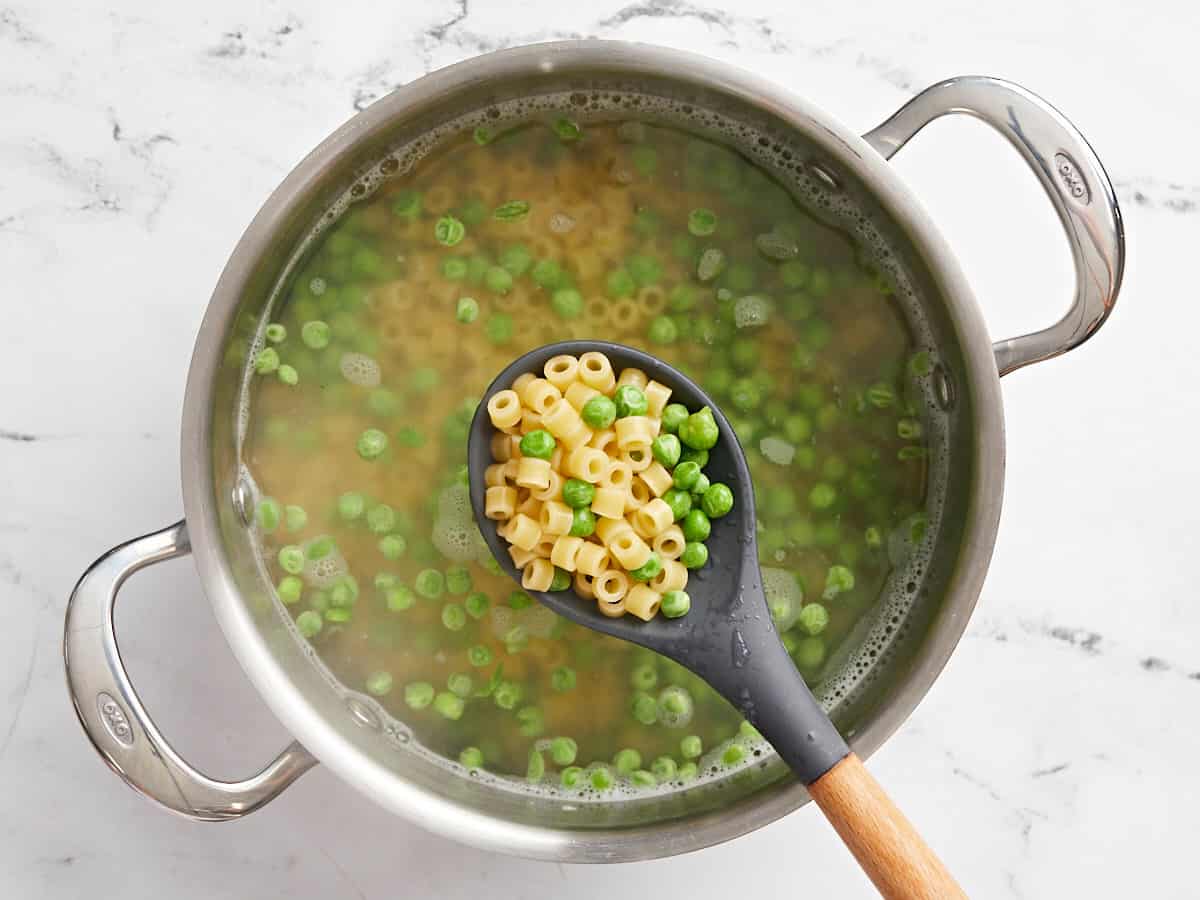 Cooked pasta and peas in a pot with a spoon lifting some out of the water.