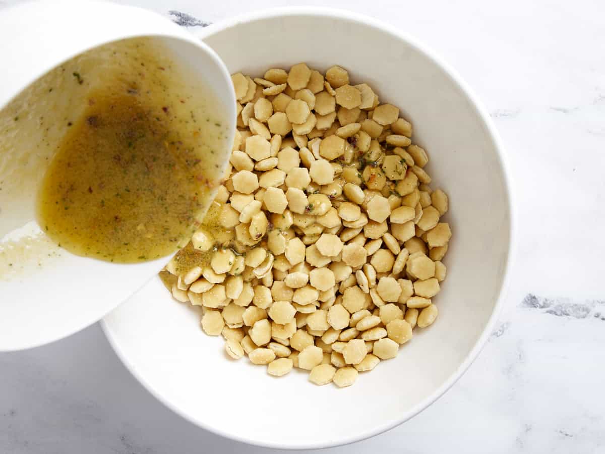 Melted butter mixture being poured over oyster crackers in a bowl.