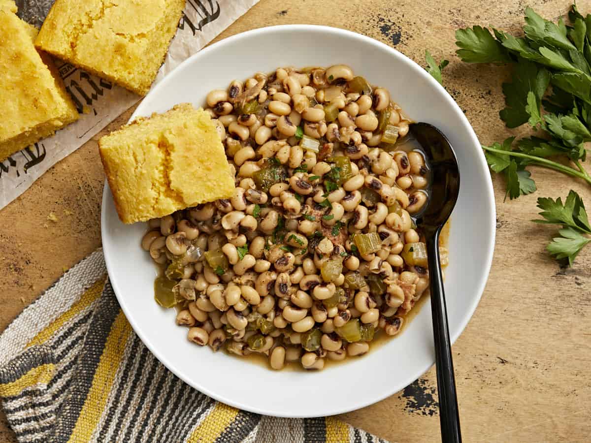 Overhead view of a bowl of black-eyed peas with a piece of cornbread on the side.