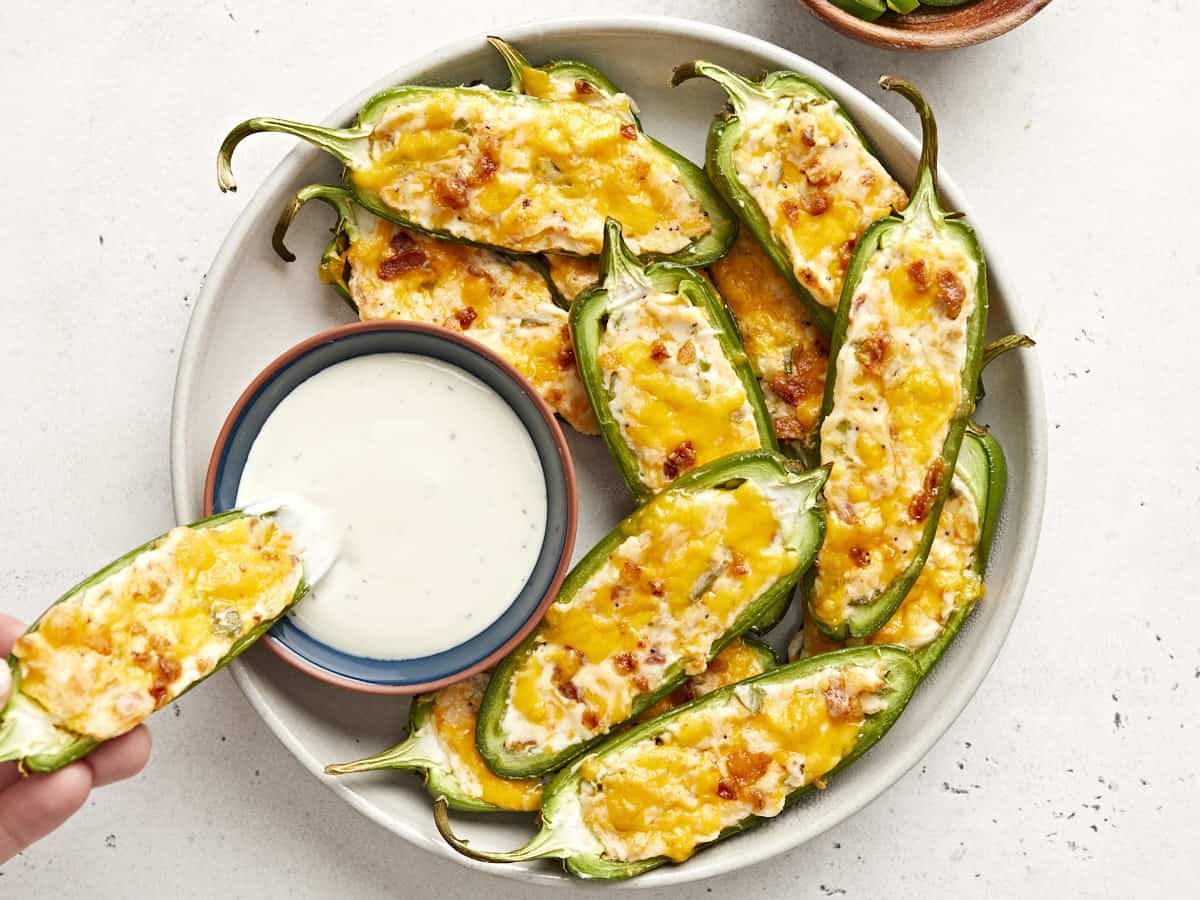 Overhead view of a plate of jalapeño peppers with one being dipped into a bowl of ranch.