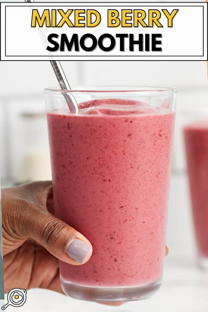 Front side view of a mixed berry smoothie in a glass being held by a hand.