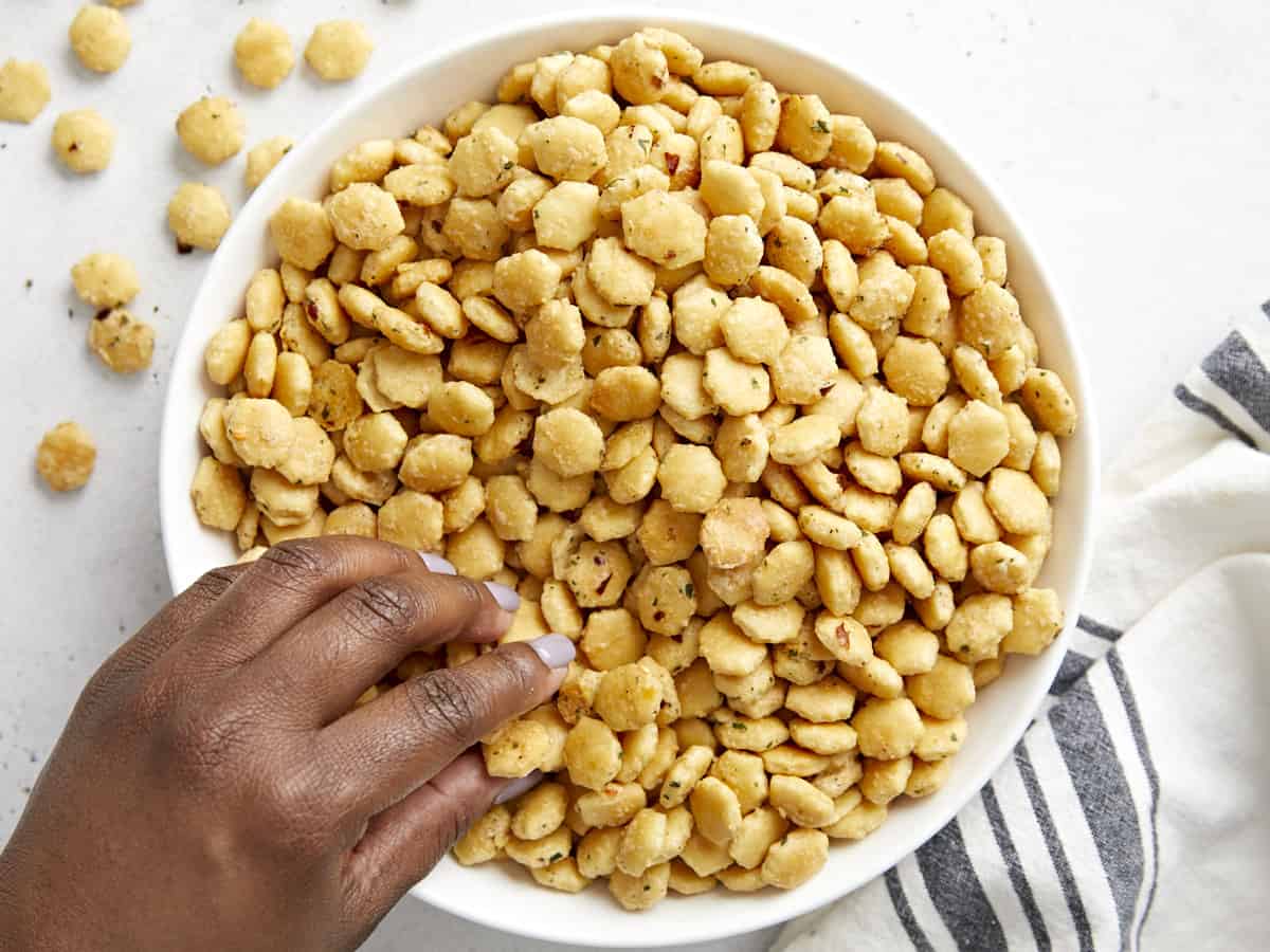 Ranch oyster crackers in a white serving bowl with a hand grabbing a few out.